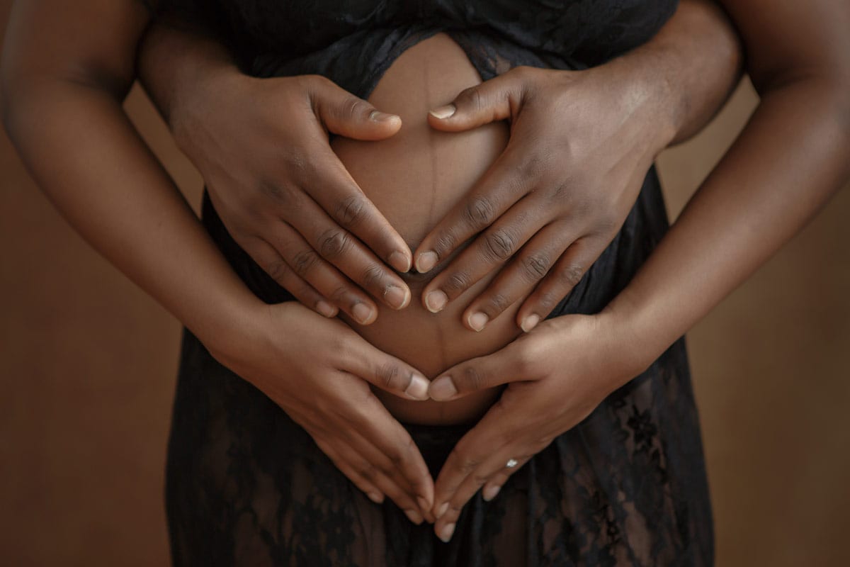 Haende der schwangeren Frau und Partner am Babybauch waehrend eines Babybauch Fotoshootings von Donna Bellini Berlin