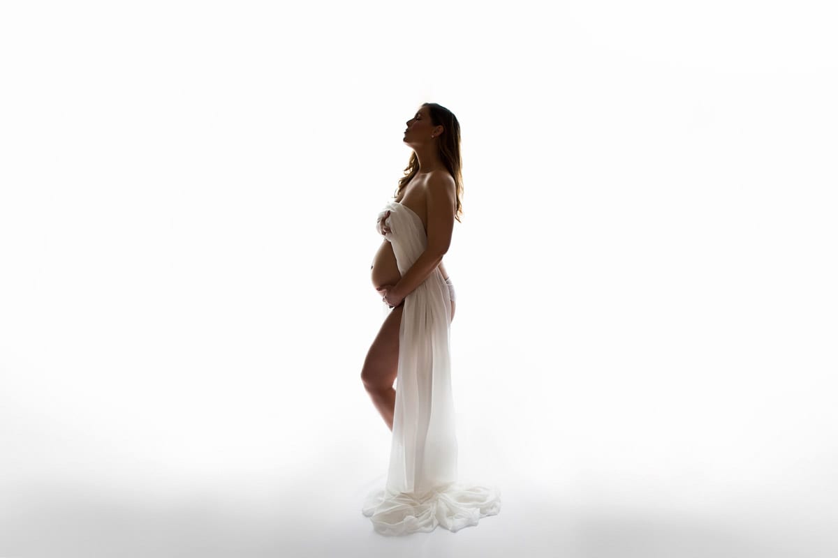Schwangere Frau mit weissem Kleid posiert vor weissem Hintergrund ein Schwangerschaftsfotoshooting von Donna Bellini Berlin