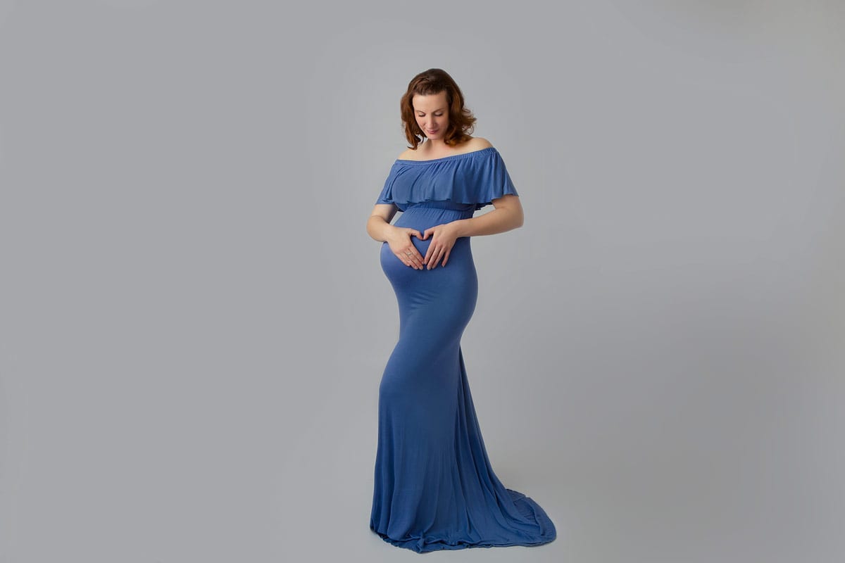 schwangere Frau posiert und macht ein Herz mit ihren Händen auf ihrem Babybauch waehrend eines Schwangerschafts-Fotoshootings im Donna Bellini Studio Berlin