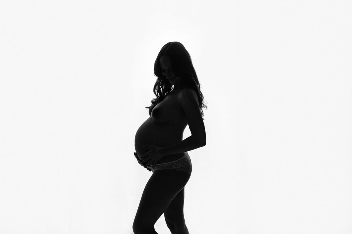 Schwangere Frau posiert fuer Schwangerschaftsfotos vor weissem Hintergrund fuer Lichts und Schatten beim Babybauch Shooting von Donna Bellini Berlin